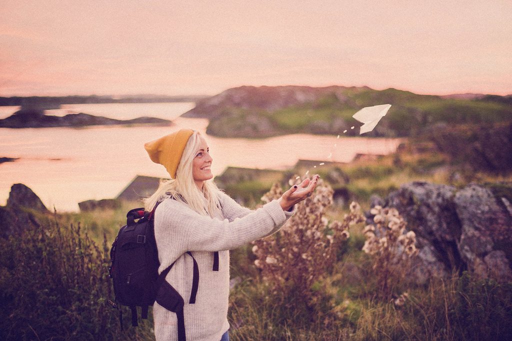 Una persona lanza un avión de papel en mitad de la naturaleza.
